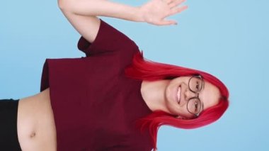 Vertical video. Goodbye gesture. Leaving farewell. Meeting end. Cheerful redhead woman waving hand bye on blue background seamless loop.