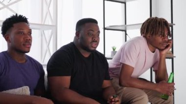 Scary video. Terrified men. Home meeting. Shocked funny male friends looking horror movie sitting together with beer in light room interior.