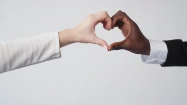 Office dating. Diverse love. Corporate relationship. Unrecognizable multiethnic man woman holding hands shaping heart gesture on white background.