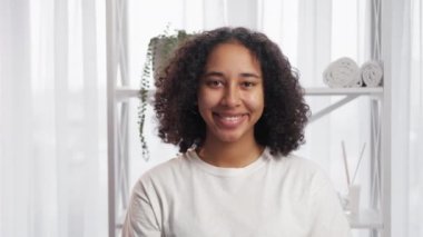 Morning beauty. Natural face. Health wellbeing. Happy smiling candid girl with fresh skin dark curly hair in light bathroom interior.