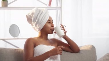 Morning inspiration. Spa weekend. Wellbeing rest. Relaxed happy smiling woman in white towel enjoying drinking tea after shower in light interior with free space.