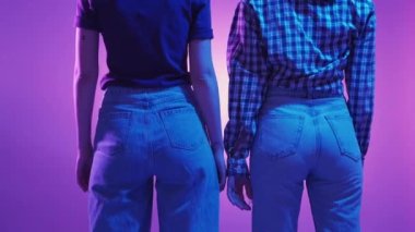 Aşkı saklamak. Lgbt ilişkisi. Neon ışıklı kadınlar. Tanımlanamayan kadın çift el ele tutuşuyor. Utanç duyuyorlar. Mavi menekşe arkaplanı..