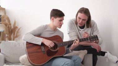 Müzik çalar. İlham veren erkekler. Yeni akoru çalış. Aydınlık odada kanepede oturan meraklı arkadaşına gitar çalmayı öğreten sıradan bir adam..