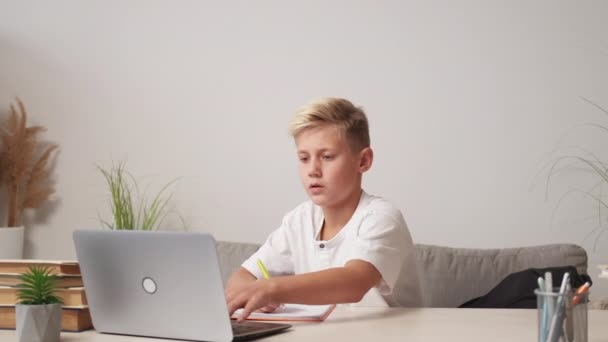 ネットワーク検索 推測された少年 宿題の勉強 笑顔ティーネージャー子供スクロールラップトップ見つける答え上のタスク座ってデスクライトルームインテリア — ストック動画