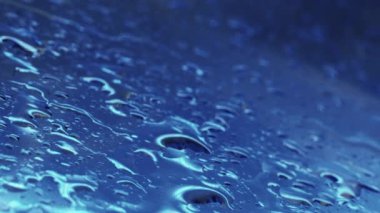 Yağmurlu bir pencere. Su damlaları. Soyut arkaplan. Parlak mavi cam yüzey makrosu üzerine düşen yağmur damlaları.