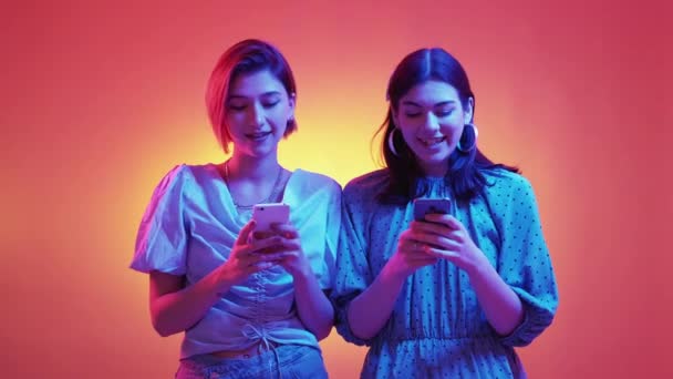 仮想ゲーム 優勝した女性 ネオンライトの人々 興奮した女性の友人正のニューススクロールスマートフォンを取得5紫色のオレンジの背景を与える — ストック動画