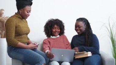 Online education. Female students. Study together. Inspired black women searching on laptop information sitting with books smartphone light room interior.