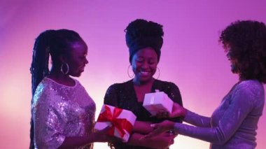 Doğum günü hediyesi. Heyecanlı kadınlar. Neon ışığı insanları. Mavi mor arka planda poz veren arkadaşlarından hediye kutusu alan harika bir kadın..