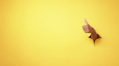 Jest gibi. Mükemmel seçim. Onay evet. Kadın el, sarı delikte baş parmağını göstermeyi öneriyor. Reklam alanı arka planında yırtık kağıt duvar..