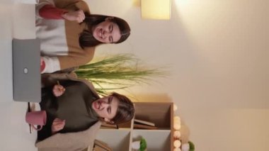 Dikey video. Harika bir sonuç. - Kız öğrenci. Ev ödevi. Heyecanlı kadınlar, birlikte karar aldıklarını ifade ediyorlar. Laptopta, aydınlık odada oturuyorlar..