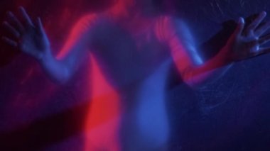 Trapped child. Defocused silhouette. Freedom isolation. Red blue neon light scared small girl hands touching creased texture transparent polyethylene film on dark out of focus.