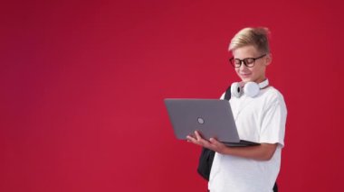Virtual meeting. Happy boy. Computer technology. Positive teenager kid holding laptop greeting online friend posing red background copy space.