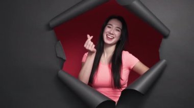 Sending love. Happy woman. Positive portrait. Smiling flirting female showing heart sign with fingers and shape gesture with hands posing red black disrupted paper frame.
