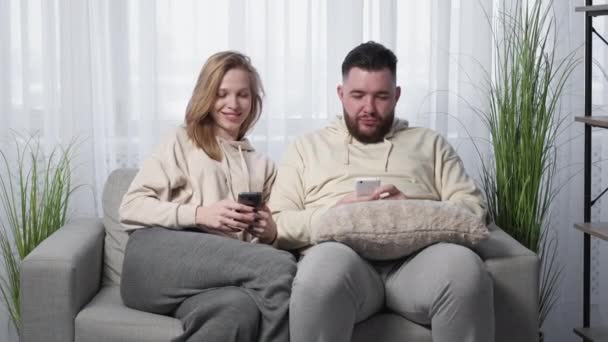 モバイルゲーム リラックスしたカップル ホームエンターテイメント 幸せな女性ショーショックマン成功でスマートフォンをプレイ楽しいです一緒に光の部屋のインテリア — ストック動画