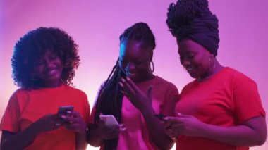 Digital life. Female friends. Neon light people. Positive black women scrolling typing smartphone posing blue purple background.