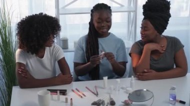 Beauty consultation. Female friends. New product. Inspired happy black women testing smelling decorative cosmetic sitting home desk in light room interior.