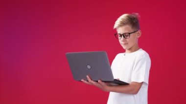 Online communication. Smart boy. Digital technology. Happy teenager kid typing laptop on red background copy space.