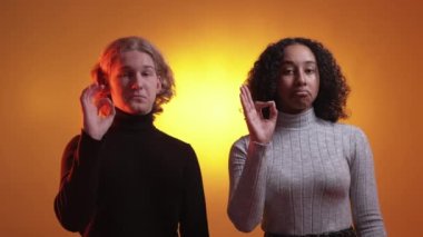 Agreed gesture. Accepted couple. Neon light people. Assured man and woman showing okey sign posing orange yellow background.