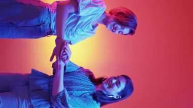 Vertical video. Female friendship. Hands unity. Neon light people. Happy women playing game putting arms together one by one purple orange background.