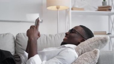 Gadget relax. Work break. Internet leisure. Joyful laughing man employee chatting online browsing phone social media resting on office sofa.