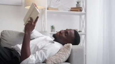 Kitap okumak rahatlatıcı. İş adamı hobisi. Ev içi rahatlık. Neşeli, konsantre bir çalışan evdeki rahat kanepede kitap dinlemenin tadını çıkarıyor..