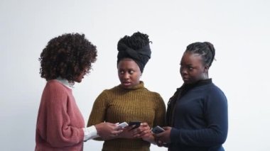 Mobile shopping. Female discussion. Digital technology. Inspired black woman showing information to surprised friends in smartphones posing light background.
