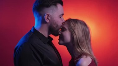 Affection feeling. Beloved couple. Neon light people. Tender man kissing happy woman on forehead embracing together on dark shadow orange blue background.