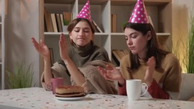 Boring party. Displeased women. Birthday fail. Disappointed female friends clapping hands with sad face looking lonely cake sitting light room interior.