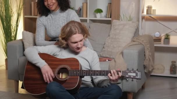 浪漫的音乐 放松的夫妇 家庭休闲 快乐的心爱的女人喜欢男朋友弹奏吉他 坐在明亮房间的地板上 — 图库视频影像