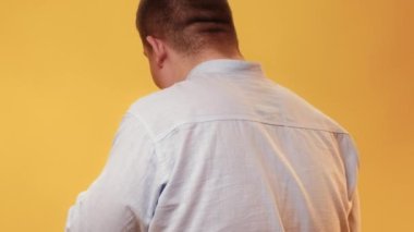 Body shaming. Obese man. Unhealthy food. Hiding plus size guy turning back eating with satisfaction chips isolated yellow background.