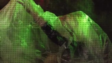 Stop pollution. Conceptual woman art. Ecology problem. Calm lady putting off transparent polyethylene film behind cell net neon light red green background.