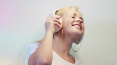 Music energy. Sound inspiration. Audio gadget. Relaxed happy smiling blonde girl in headphones enjoying listening to mp3 dancing on light pastel color gradient background.