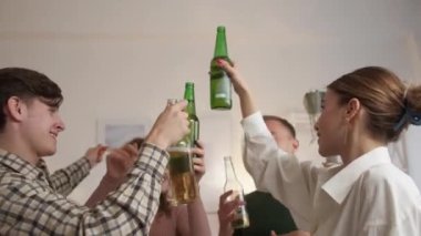 Drink party. Happy friends. Music joy. Relaxed men and women dancing together cheering bottles of beer in light room interior.