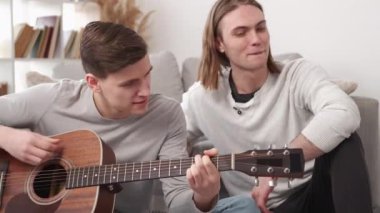 Music joy. Male player. Home leisure. Inspired casual men spending good time playing guitar and singing sitting floor in light room interior.
