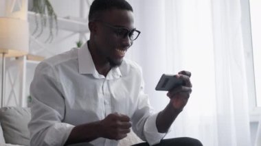 Phone game. Mobile entertainment. Office leisure. Happy man employee playing smartphone application enjoying work break on sofa.
