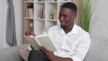 Book reading. Hobby leisure. Work recreation. Cheerful smiling man employee enjoying literature sitting comfortable sofa at home interior.