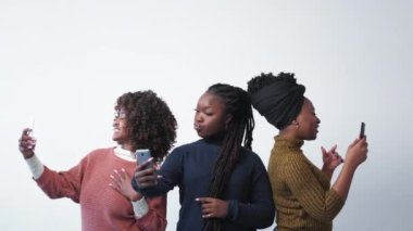 Network selfie. Digital addiction. Female friends. Pretty self-confident black women posing on mobile photo making together on light background.