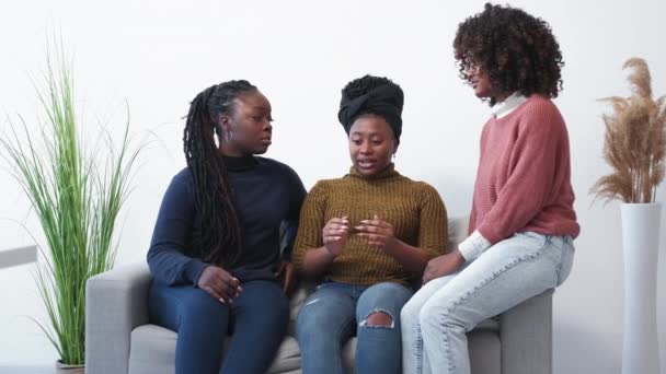 女性支持 好朋友愉快的见面 快乐的黑人女人拥抱着一个可怜的女人坐在灯光下的沙发上 — 图库视频影像