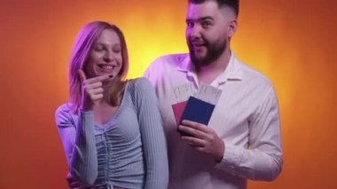 Vacation excitement. Holiday tickets. Happy couple. Inspired man and woman feeling joy holding passports with boarding pass joy posing neon light purple orange background.