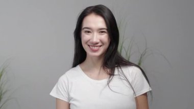 Refreshing hairstyle. Female treatment. Model shooting. Happy brunette woman with long blowing careful hair posing gray background light room interior slow motion.