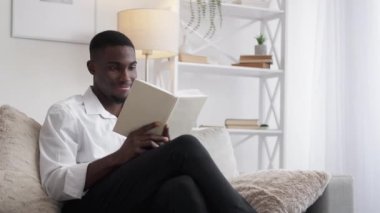 Book knowledge. Academic research. Home study. Happy surprised man reading interesting literature on cozy couch light room interior.