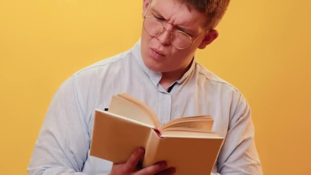 书迷肥胖的男人 令人惊讶的信息 头戴眼镜的多愁善感的大个子男人 看上去惊讶地看着黄色背景的阅读故事 — 图库视频影像