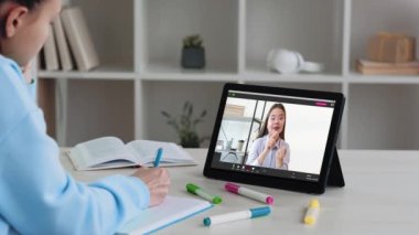 Online teaching. E-learning meeting. Remote education. Tired female student watching virtual lesson taking notes listening to coach on tablet at workplace.