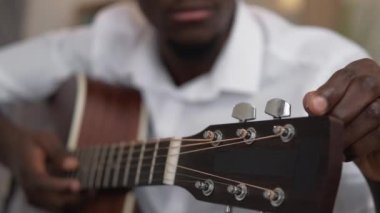 Guitar tuning. Music practice. Acoustic player. Closeup of headstock with defocused man guitarist hand adjusting string.