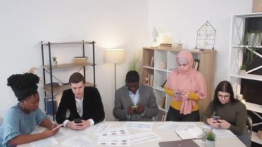 Mobile work. Office colleagues. Digital technology. Concerned estranged men and women typing personal smartphones sitting desk in light room interior.