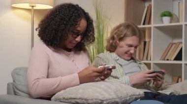 Mobile gaming. Friends leisure. Home entertainment. Excited man expressing joy winning game in upset woman playing smartphone in light room interior.