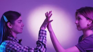 Female couple. Lgbt relationship. Neon light people. Two women holding hands together with tattoo word love on one posing green violet background.
