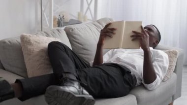 Work sleep. Couch relax. Reading break. Tired yawning man entrepreneur enjoying book resting on cozy sofa at office lobby interior.