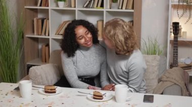 Pleasant meeting. Beloved couple. Home leisure. Happy man and woman embracing together sitting desk sweet cakes and coffee in light room interior.