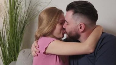 Affection love. Beloved couple. Home leisure. Happy man and woman feeling attraction kissing with passion sitting sofa in light room interior.